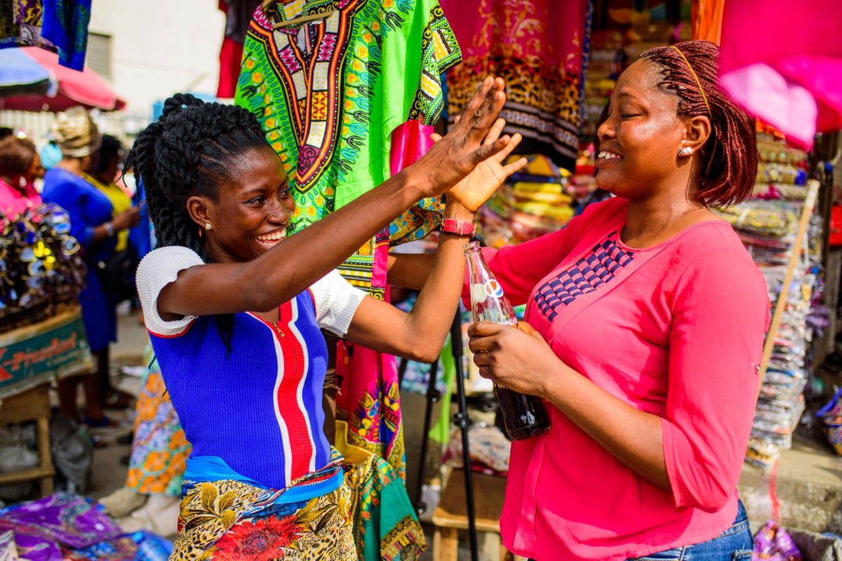 Two women at clothing stall talking.