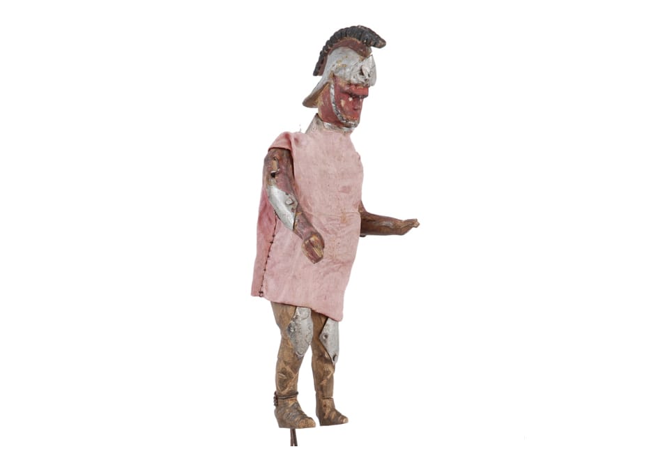 Puppet of man wearing armour on legs and arms. It is also wearing a helmet.