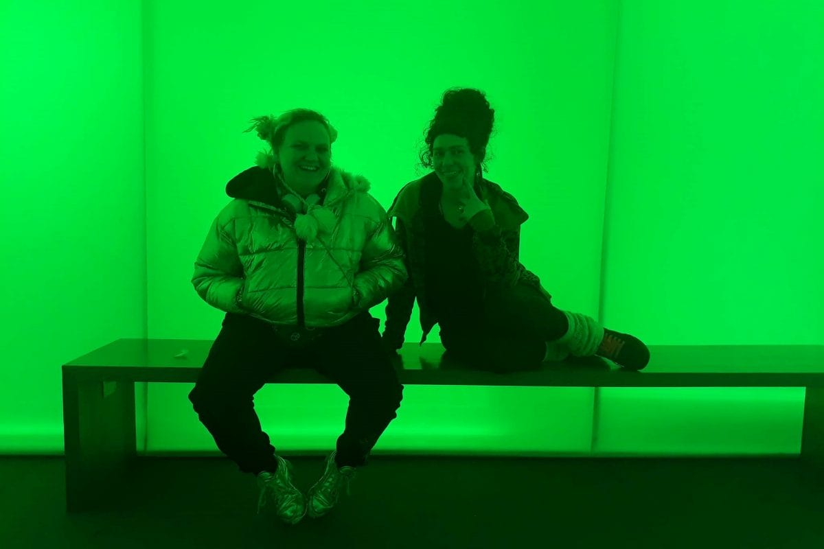 Two female teenagers sitting on bench in green lit room