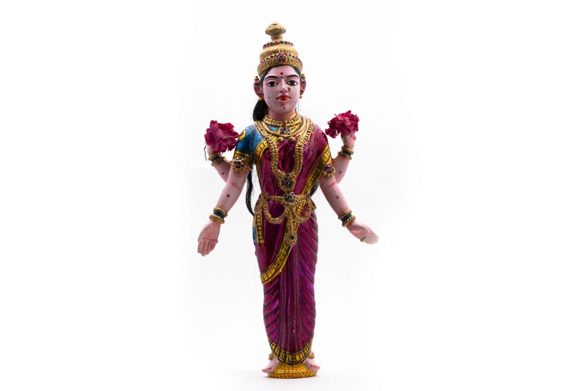 Polychrome wooden figure depicting Lakshmi wearing a purple-pink sari and holding two pink paper flowers