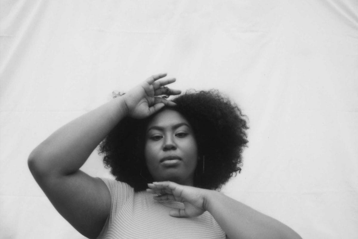 A woman holds one hand to her forehead and one to her chin as she poses against a white backdrop