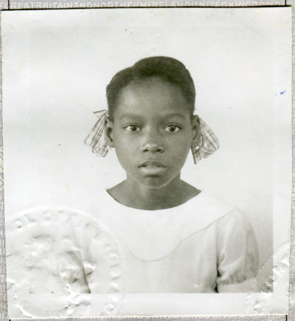 Old passport photo of a young black girl wearing a white dress and with hair in bunches