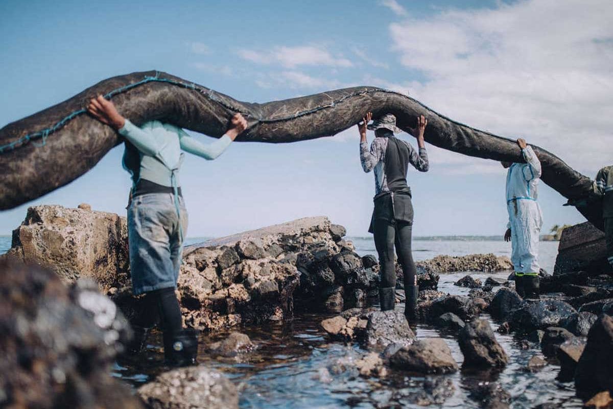 Volunteers lift a boom onto their shoulders as they stand in the water