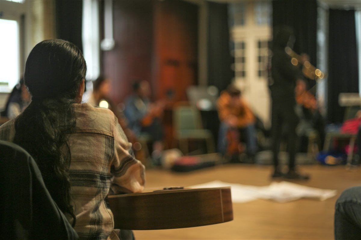 A room with people sitting in a circle, some have instruments