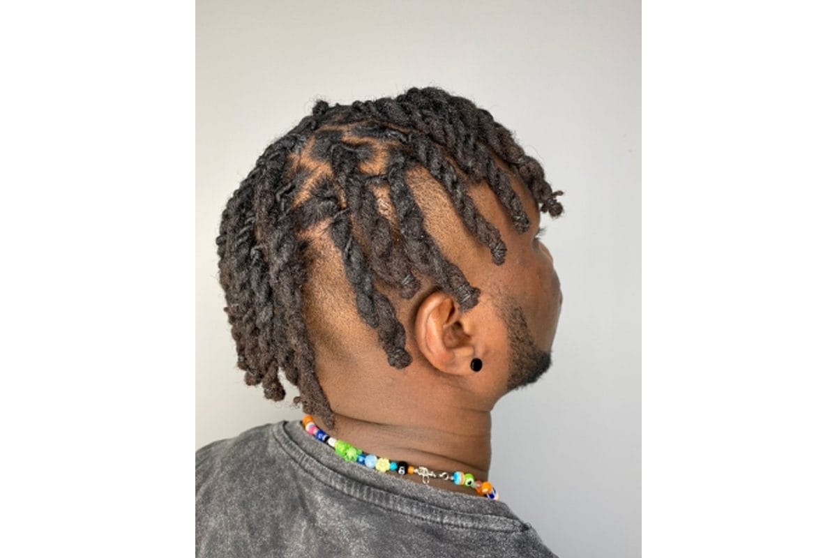 The back of a head with dreadlocks. The man has an earring and a colourful beaded necklace