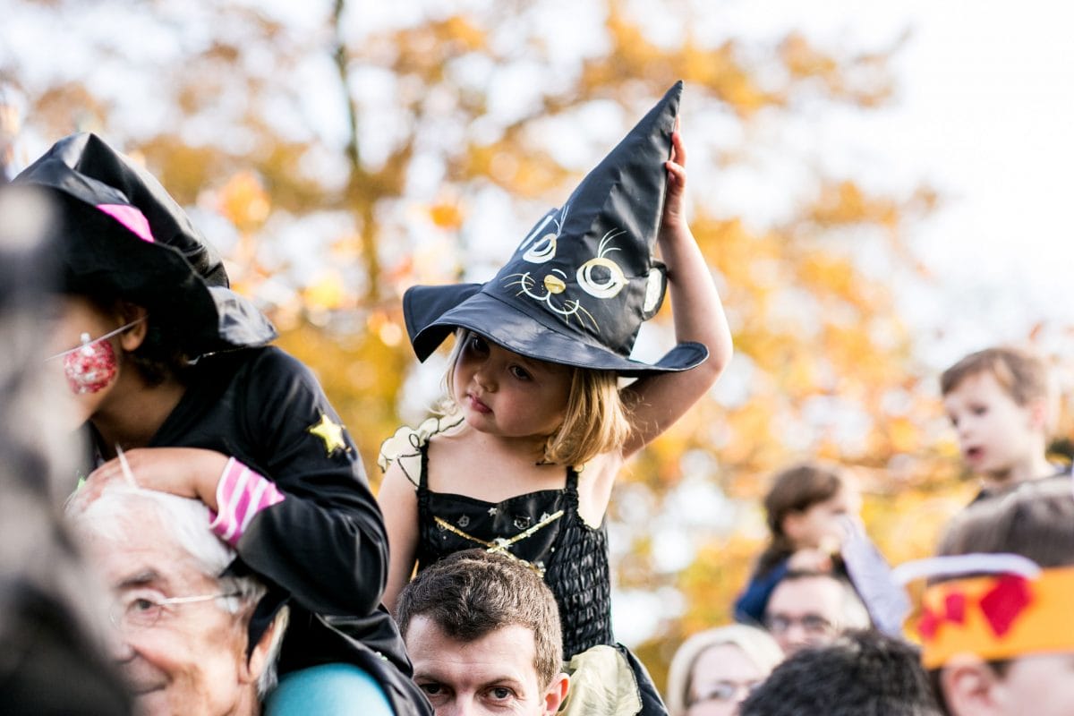 A girl wearing a witches hat on a parents shoulders