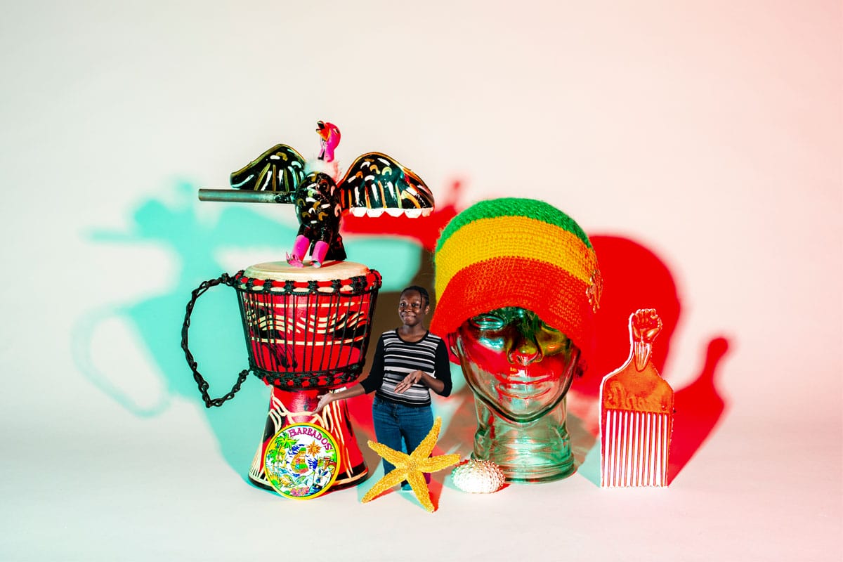 Woman standing near a starfish, drum, afro comb, and green, yellow an red striped hat