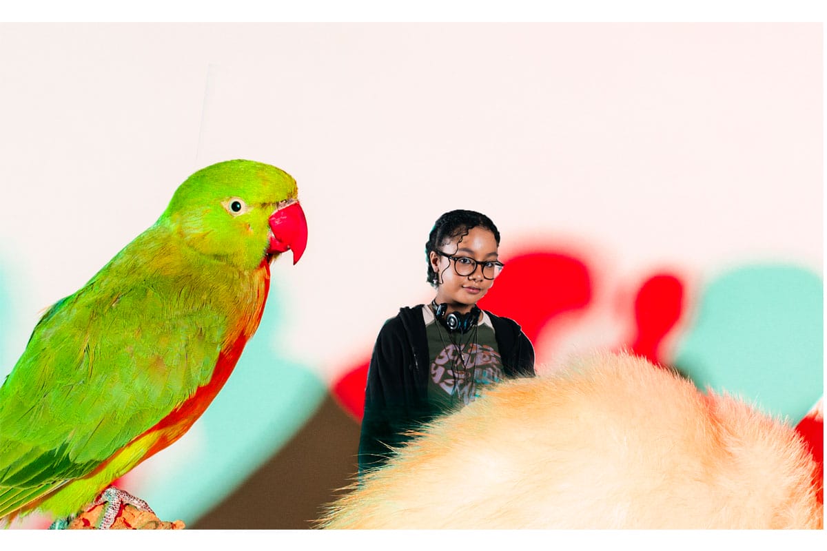 Girl wearing headphones round her neck and glasses, there is a stuffed parrot next to her