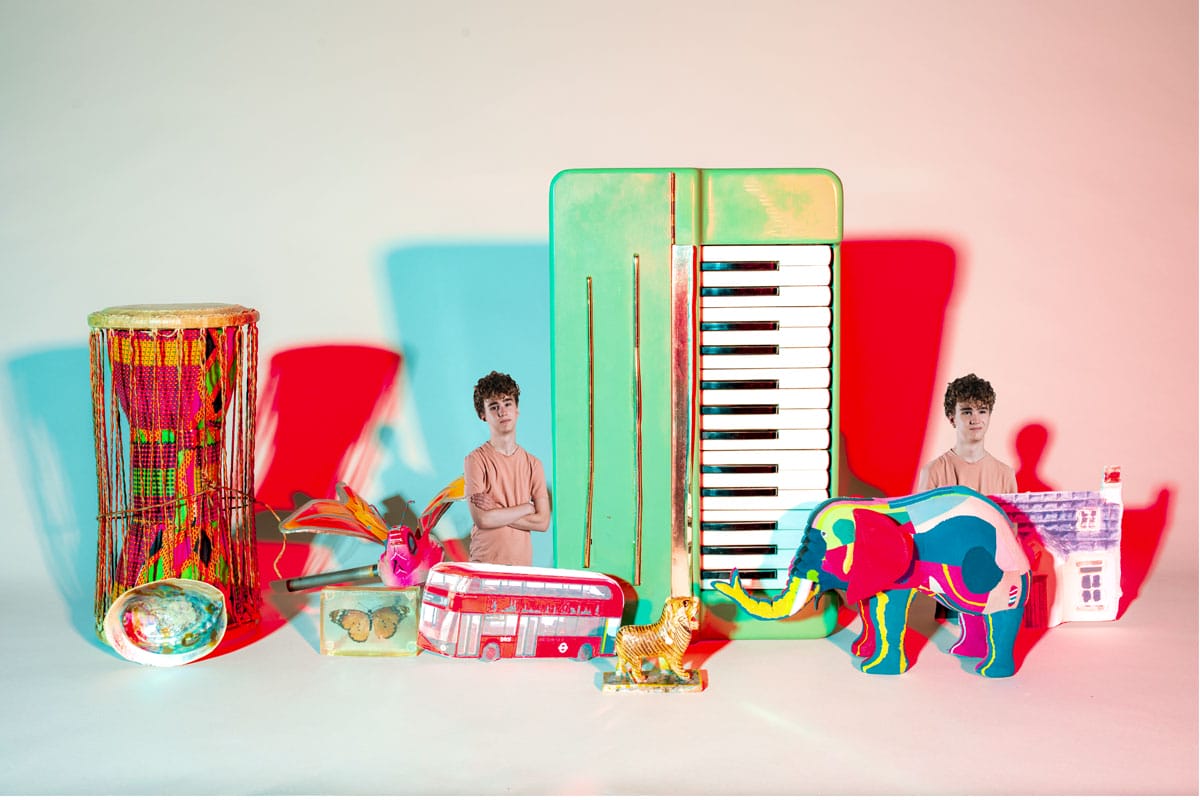 Photo of a young man edited twice into a pile of objects including a drum, a keyboard, a colourful elephant and a butterfly