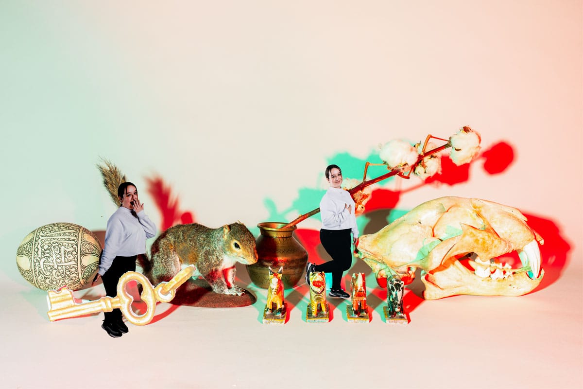 Photo of a young woman edited to look small amongst some objects including an egg, a taxidermy squirrel and an animal skull