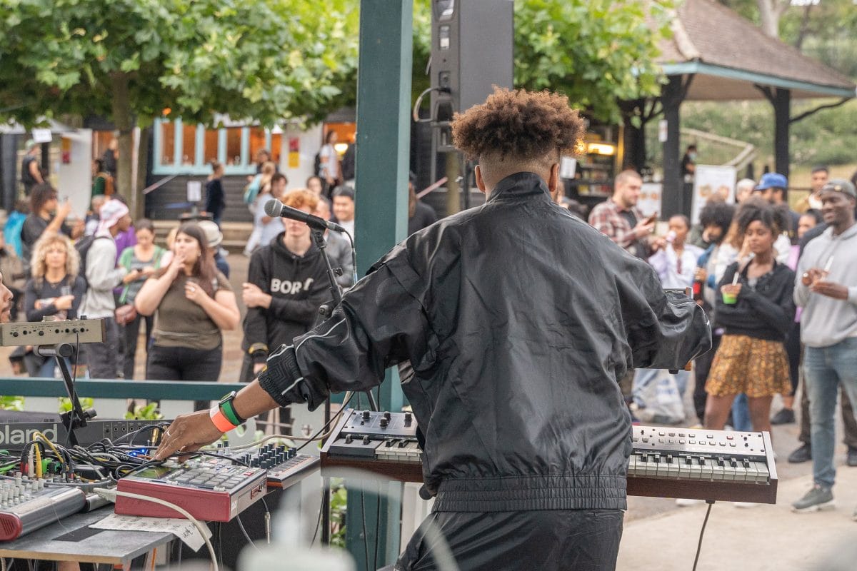 Back of a man DJing, he faces a crowd