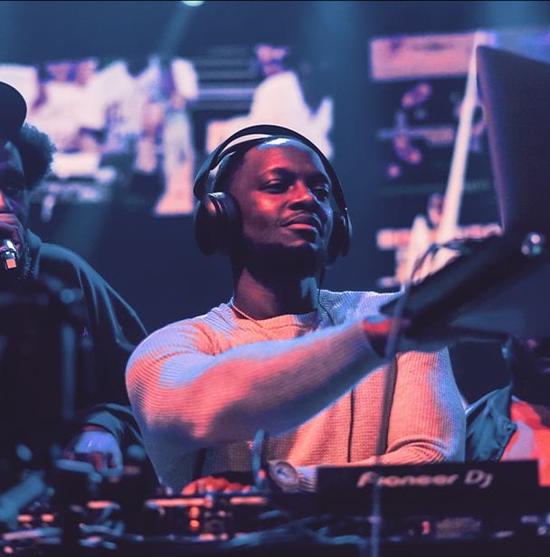 SuperMidz DJing, he is bathed in purple light and wearing headphones