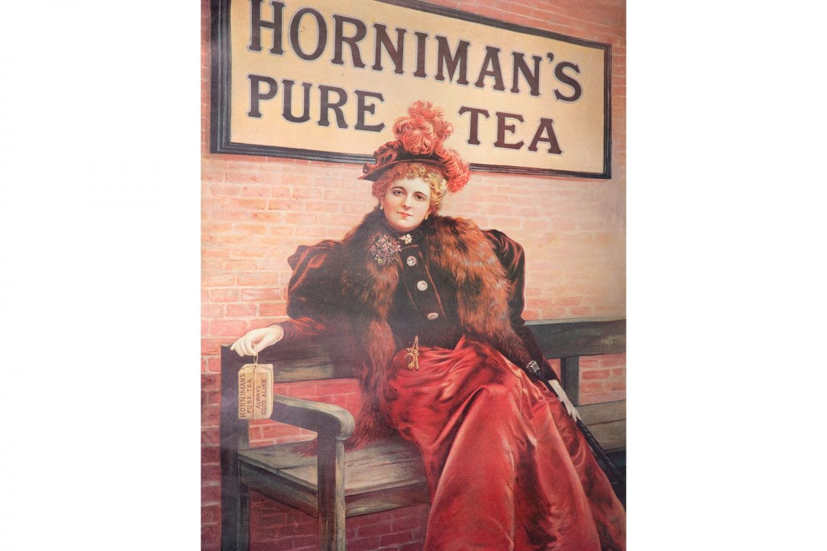 A historic advert for Horniman's Tea: a woman in Edwardian dress holds a package of Horniman's Tea in front of a Horniman's Tea sign