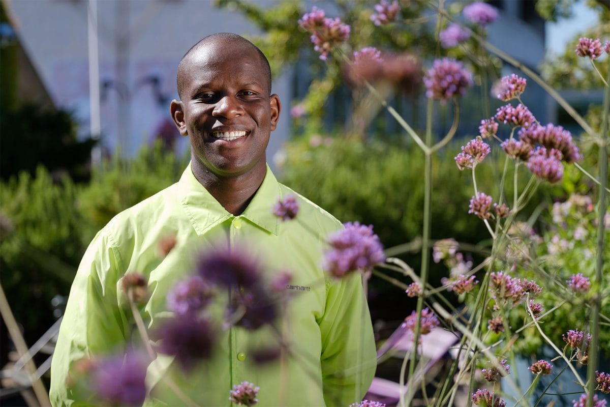 Llove Ssega smiles at the camera surrounded by purple flowers