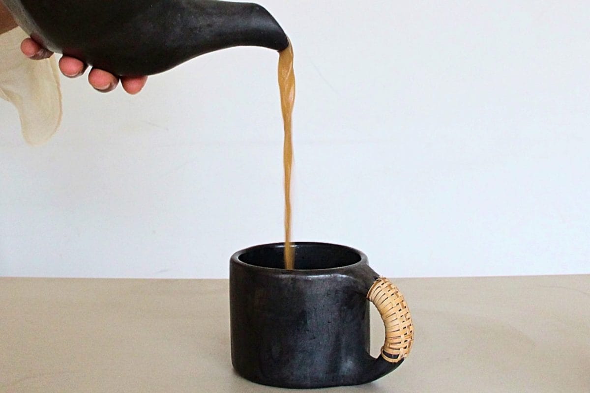 Tea being poured from a black teapot to a black mug