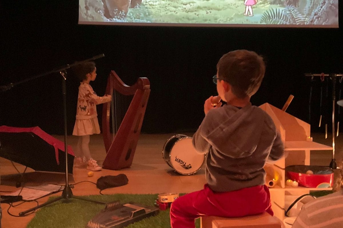 The backs of two children playing musical instruments in front of a projector playing a film