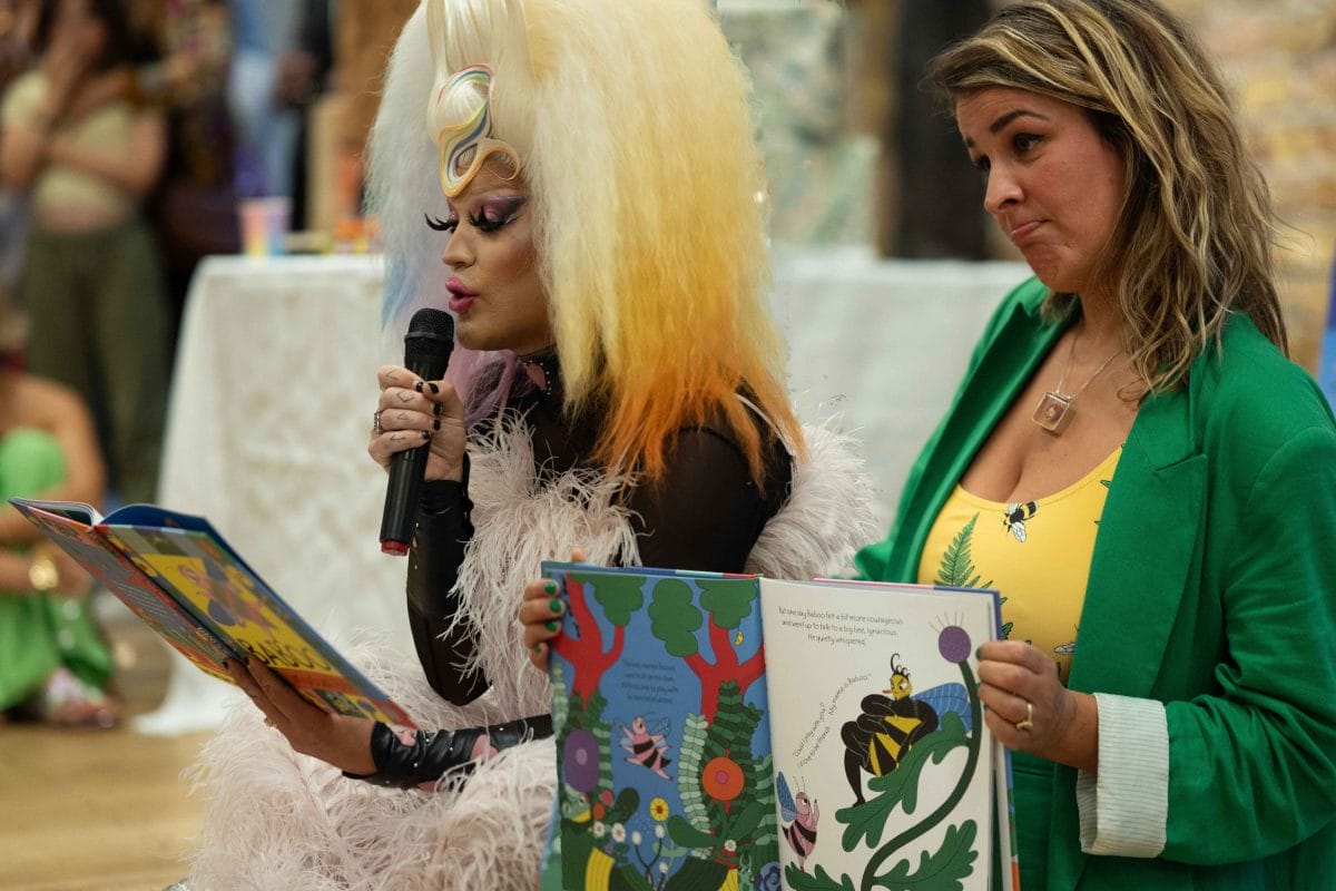 Drag queen reads from a picture book and a woman next to her holds the book open to audience