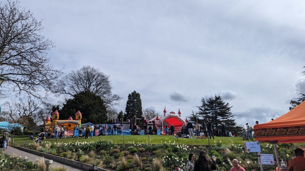 A stretch of grass with a flower bed in front of it. On the grass are three bouncy castles.