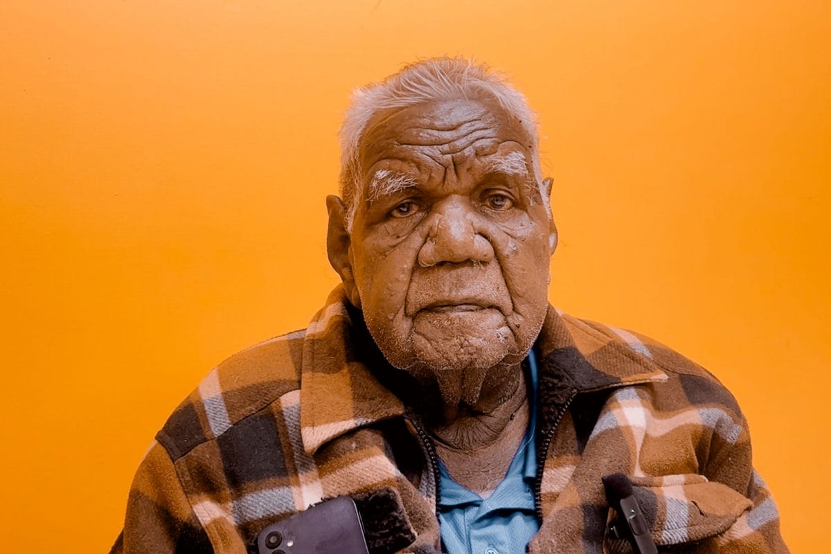 Mr Michael Jones portrait, a Warumungu senior man, sat in front of an orange background