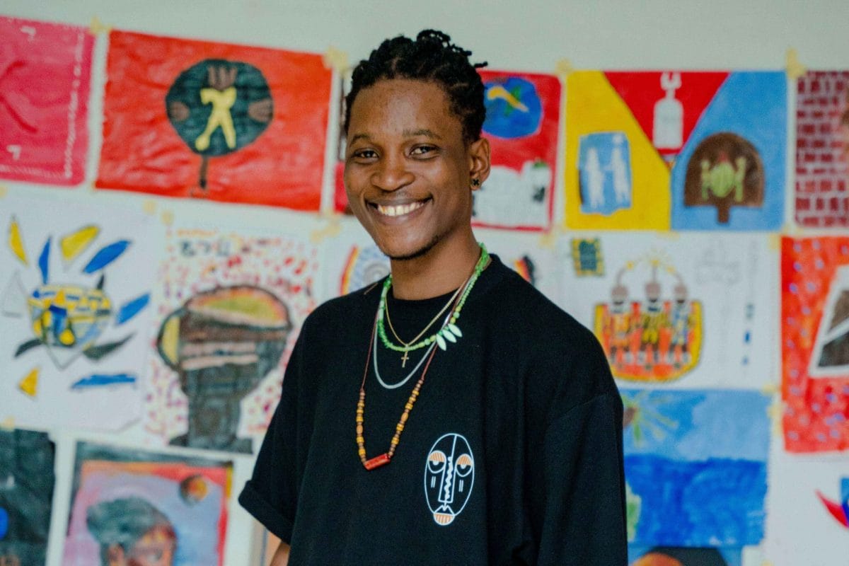 A man stands with one hand in his pocket in front of a row of children's artworks