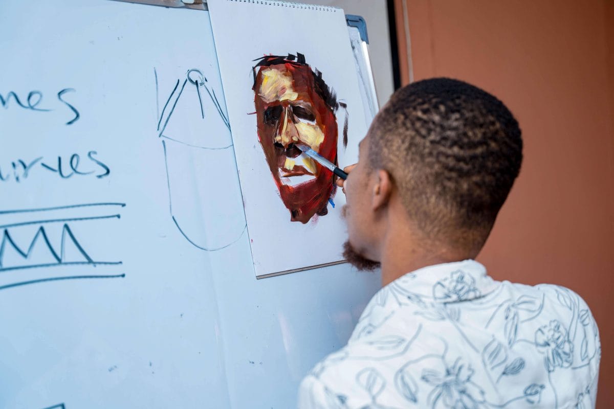 A man paints a face on a piece of paper pinned to the corner of a whiteboard