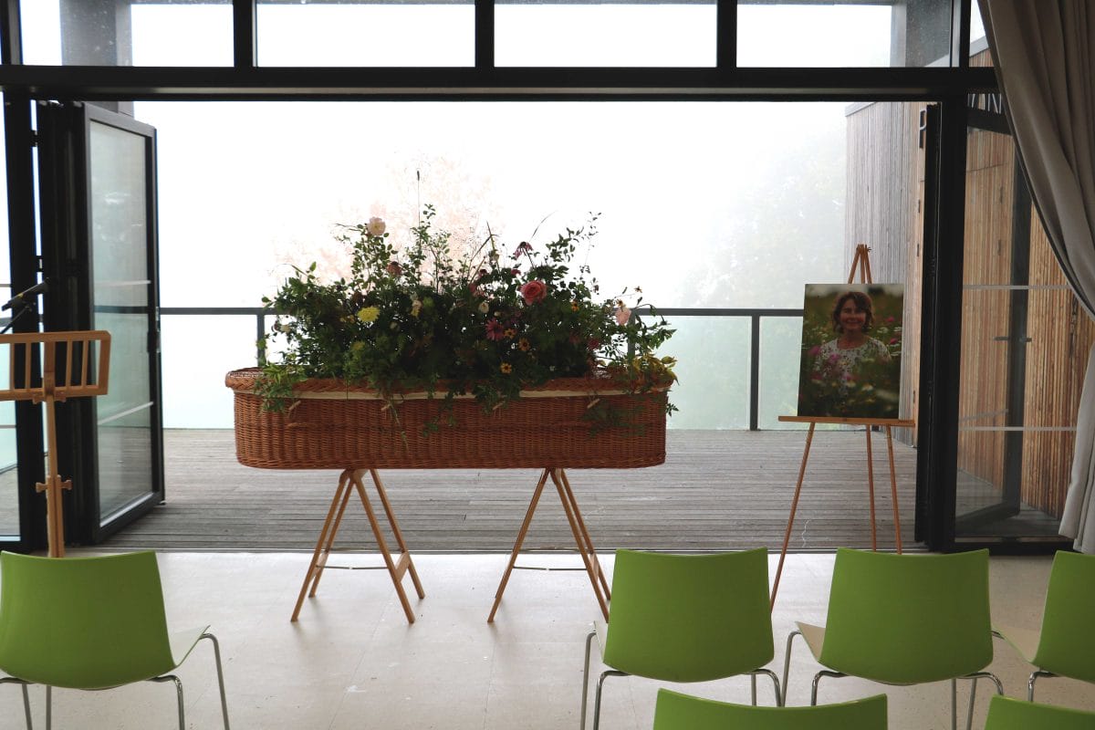 Funeral set up with wicker coffin in front of rows of chairs and a decking area behind