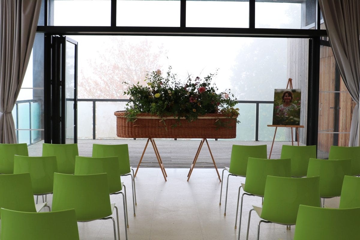 Funeral set up with wicker coffin in front of rows of chairs and a decking area behind