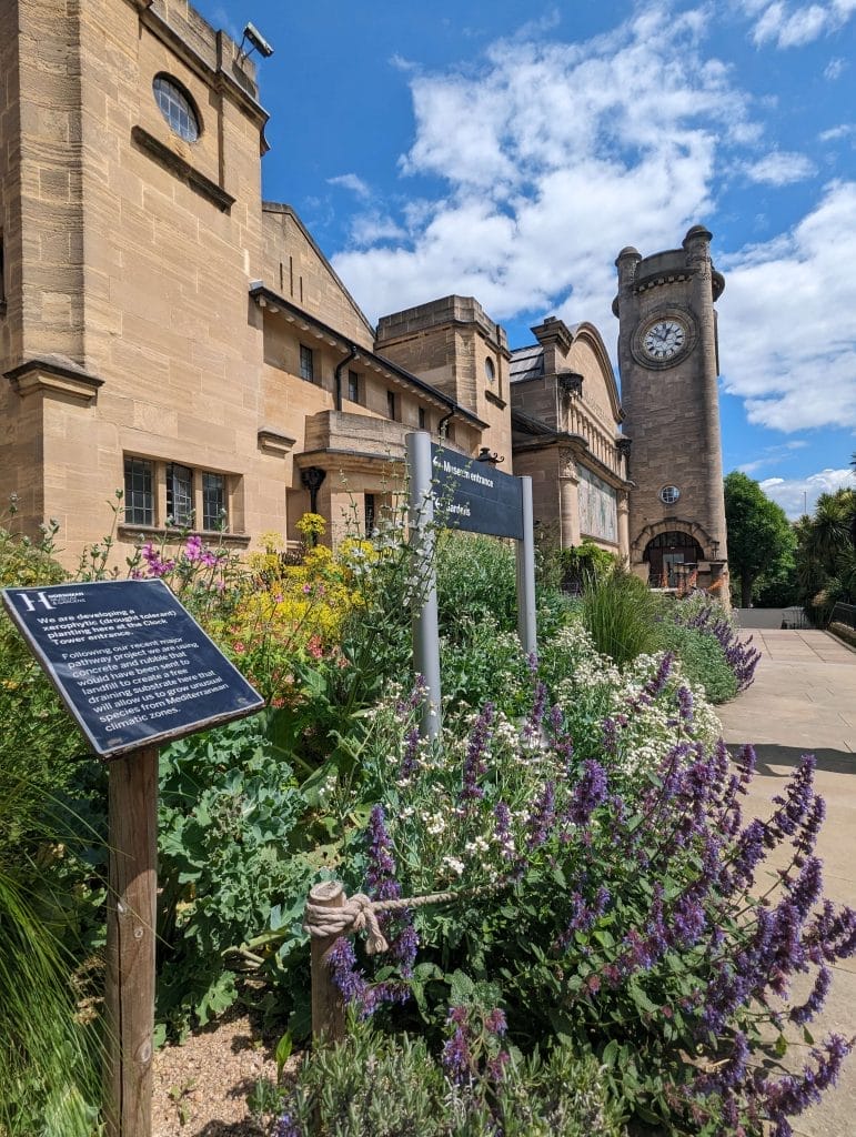 Front of Museum and clocktower with colourful climate change bed in foreground