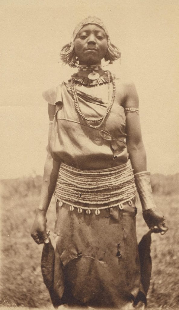 Photographic print of woman wearing long cloth attached at one shoulder, waist-ornament with beads and shells and arm-ornaments