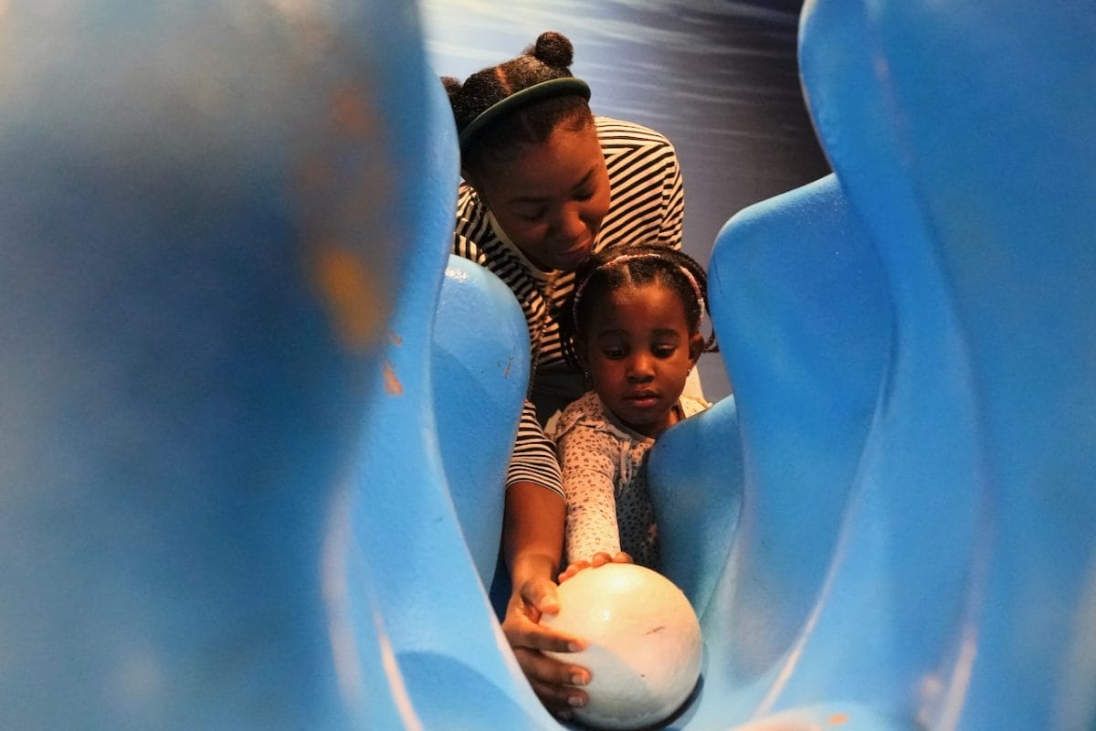 Mother and child play with a pearl figurine at the Voyage to the Deep exhibition.