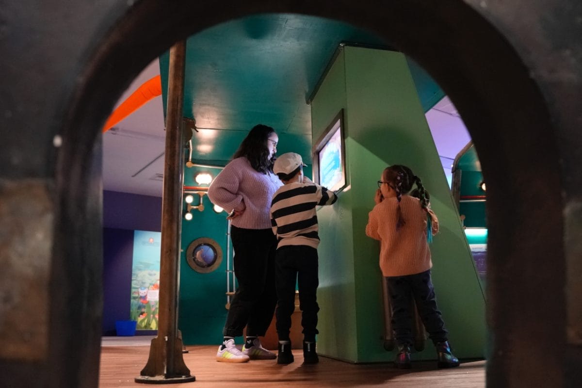 Two children and an adult read a screen prompt at the Voyage to the Deep exhibition.