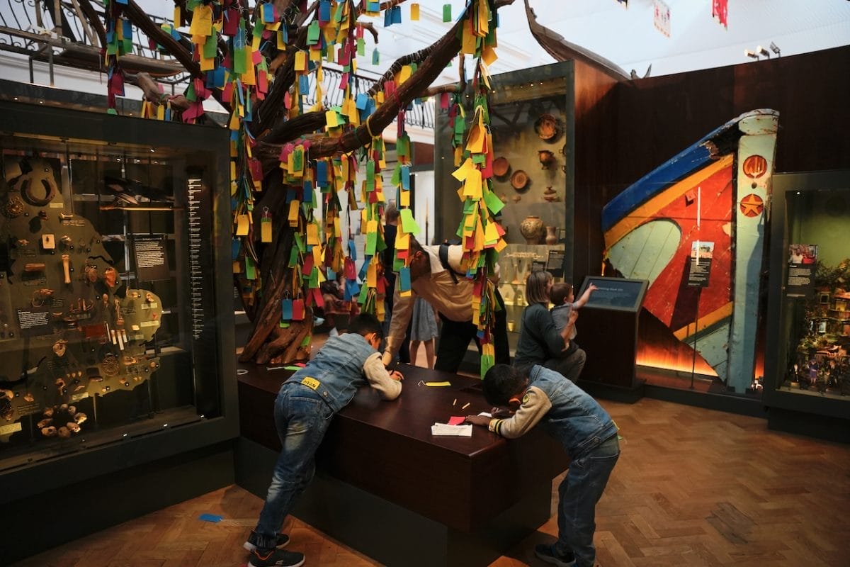 Two children write labels to go on the cloutie tree, which is behind them
