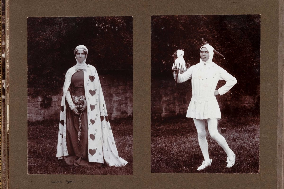 Two performers dressed in regency costumes, one a woman wearing a cape adorned with hearts and one a man dressed as a jester