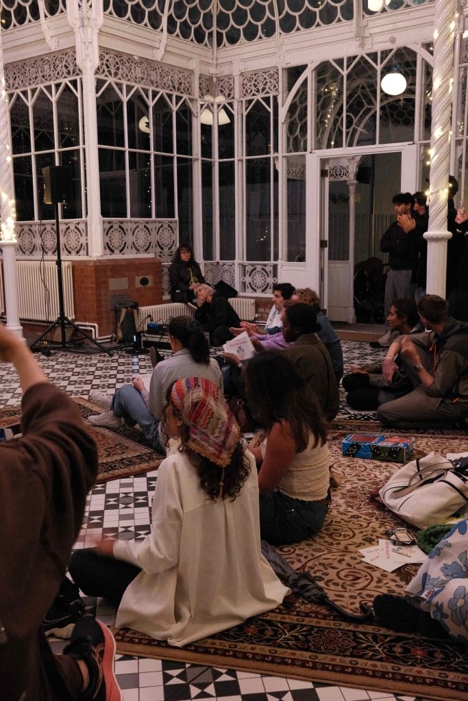 People sit on the floor in the Horniman Conservatory, some with their hands raised