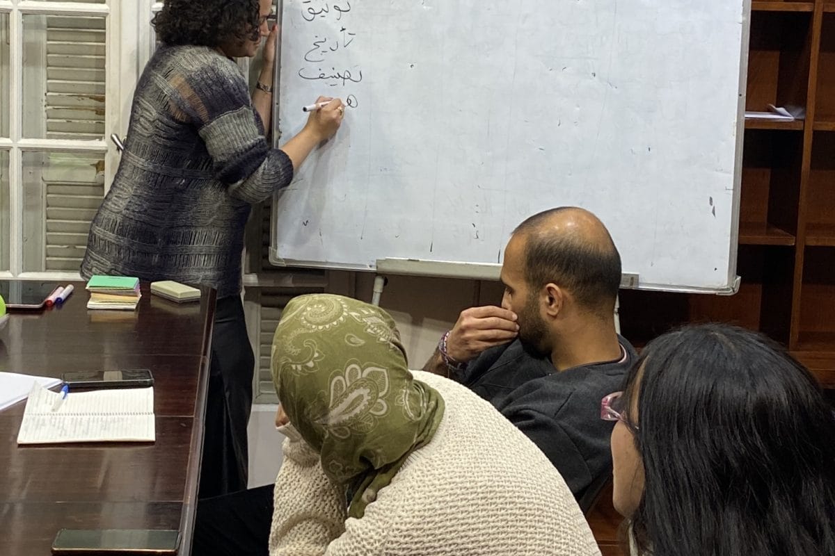 Woman writes on a workboard as people sat in front of her watch