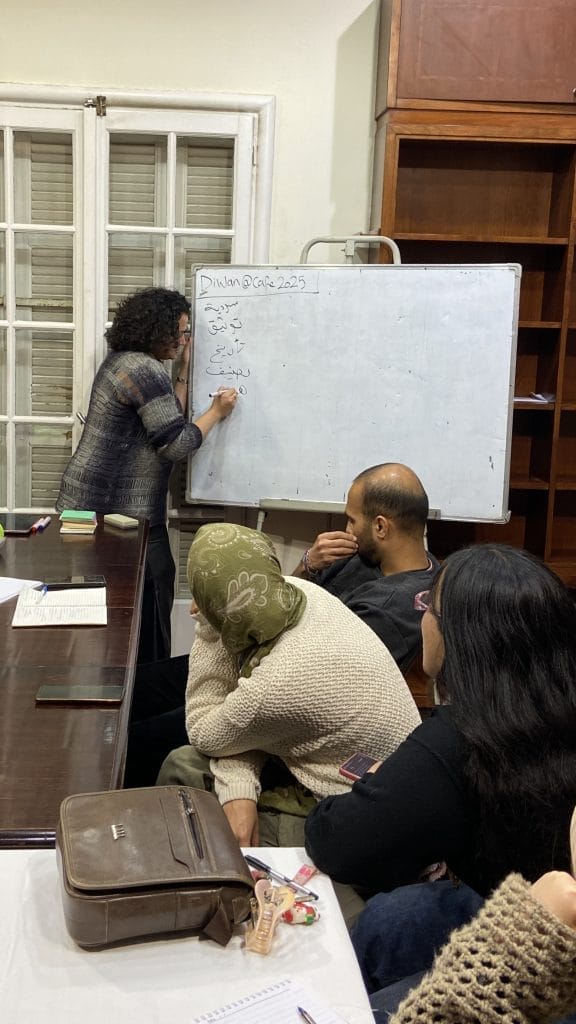 Woman writes on a workboard as people sat in front of her watch
