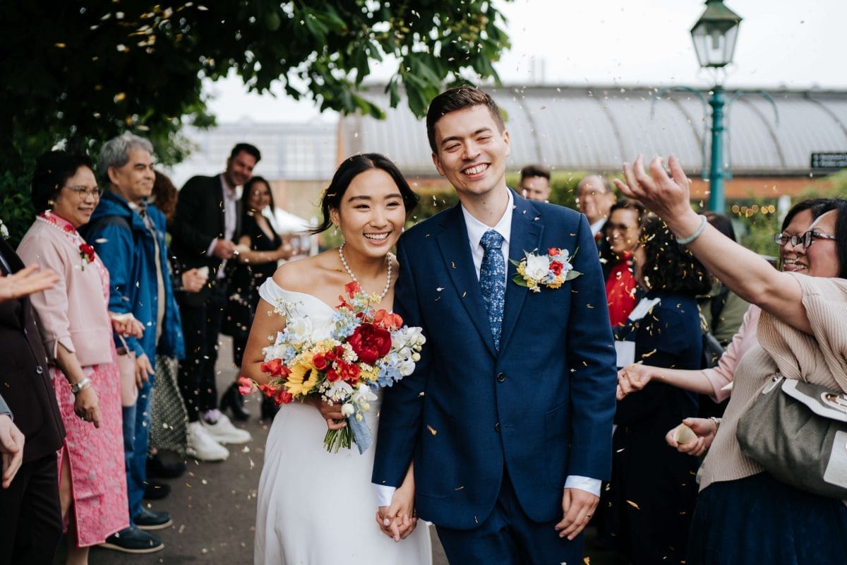 A bride and groom walk through people throwing confetti