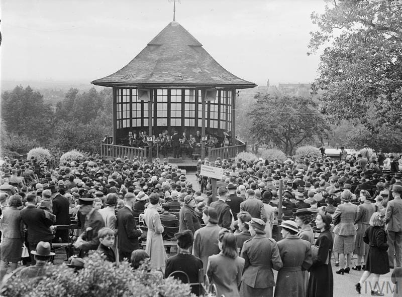 A band play on teh Bandstand with huge crowds seated before it listening