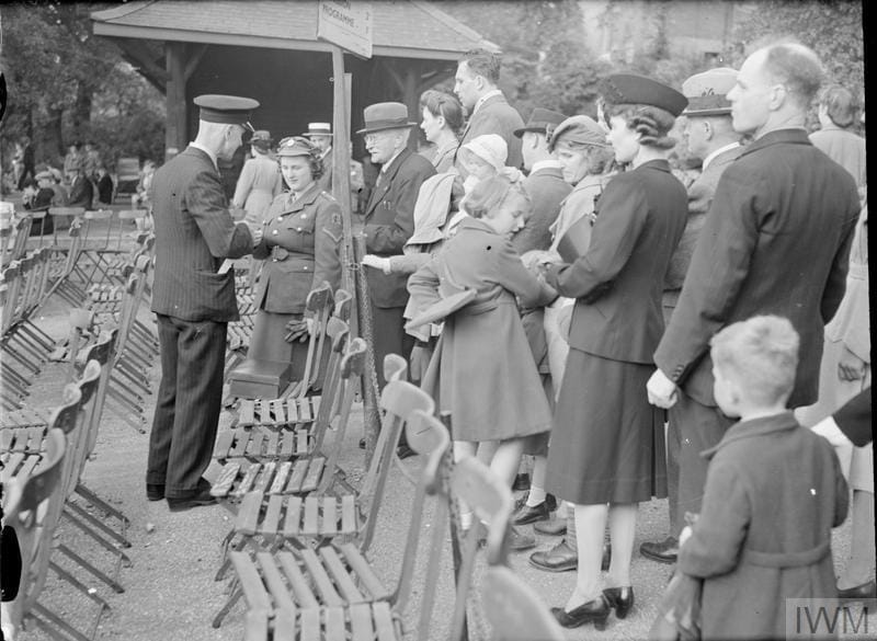 A line of men, women and children wait to purchase tickets from a man selling seats at a concert in the Horniman grounds