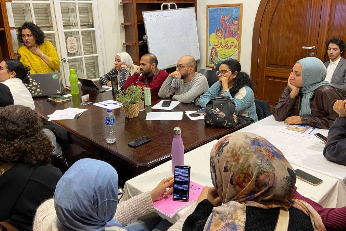 Group of people sat round a table in a workshop looking at a screen that is off camera