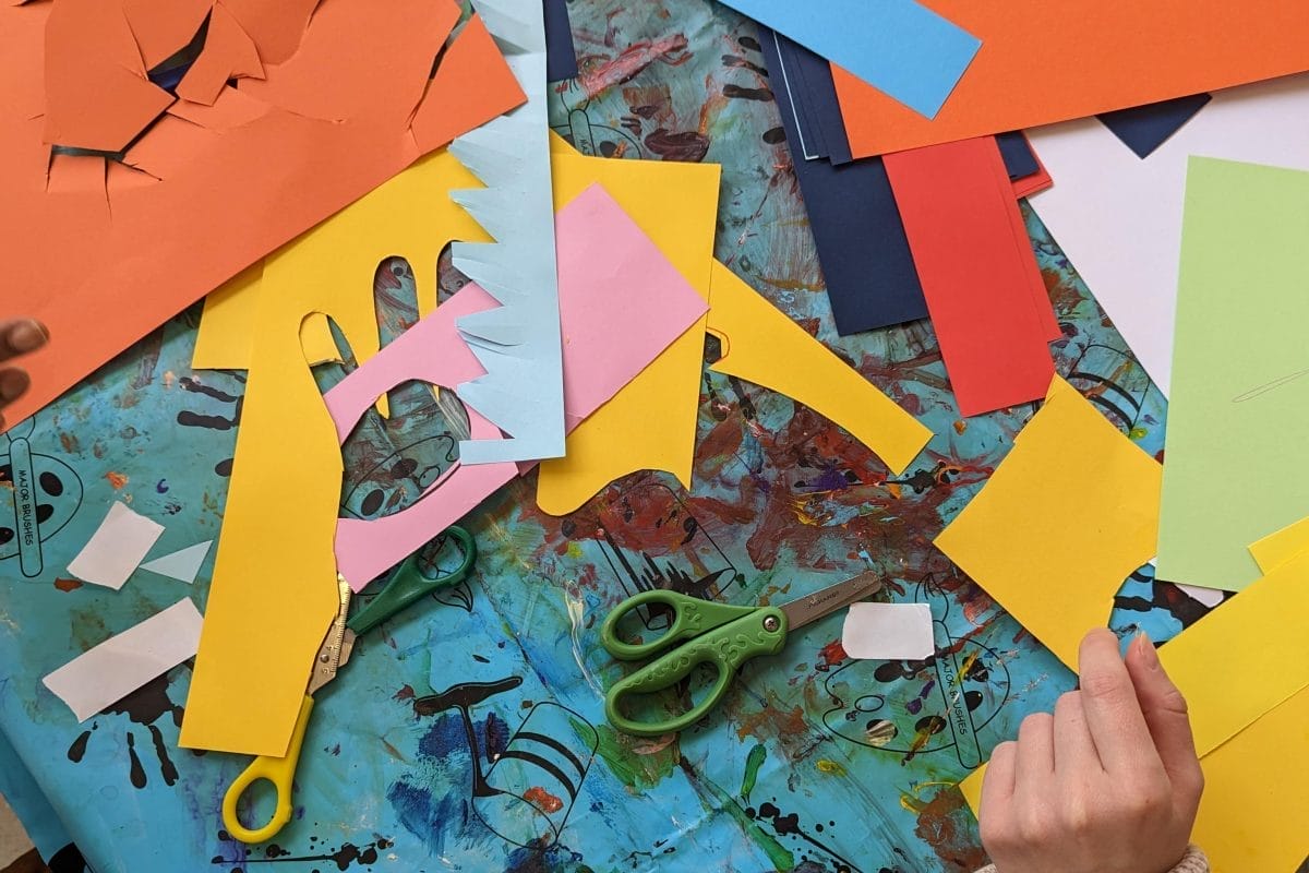 Arts and craft table , including colourful card, a table covered in paint, and childrens hands