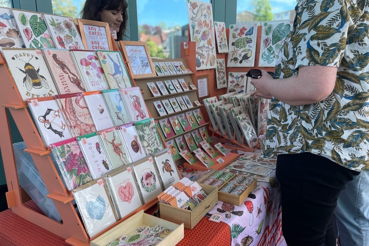 Man in floral shirt looks at crafted cards at the Horniman Sunday Market.